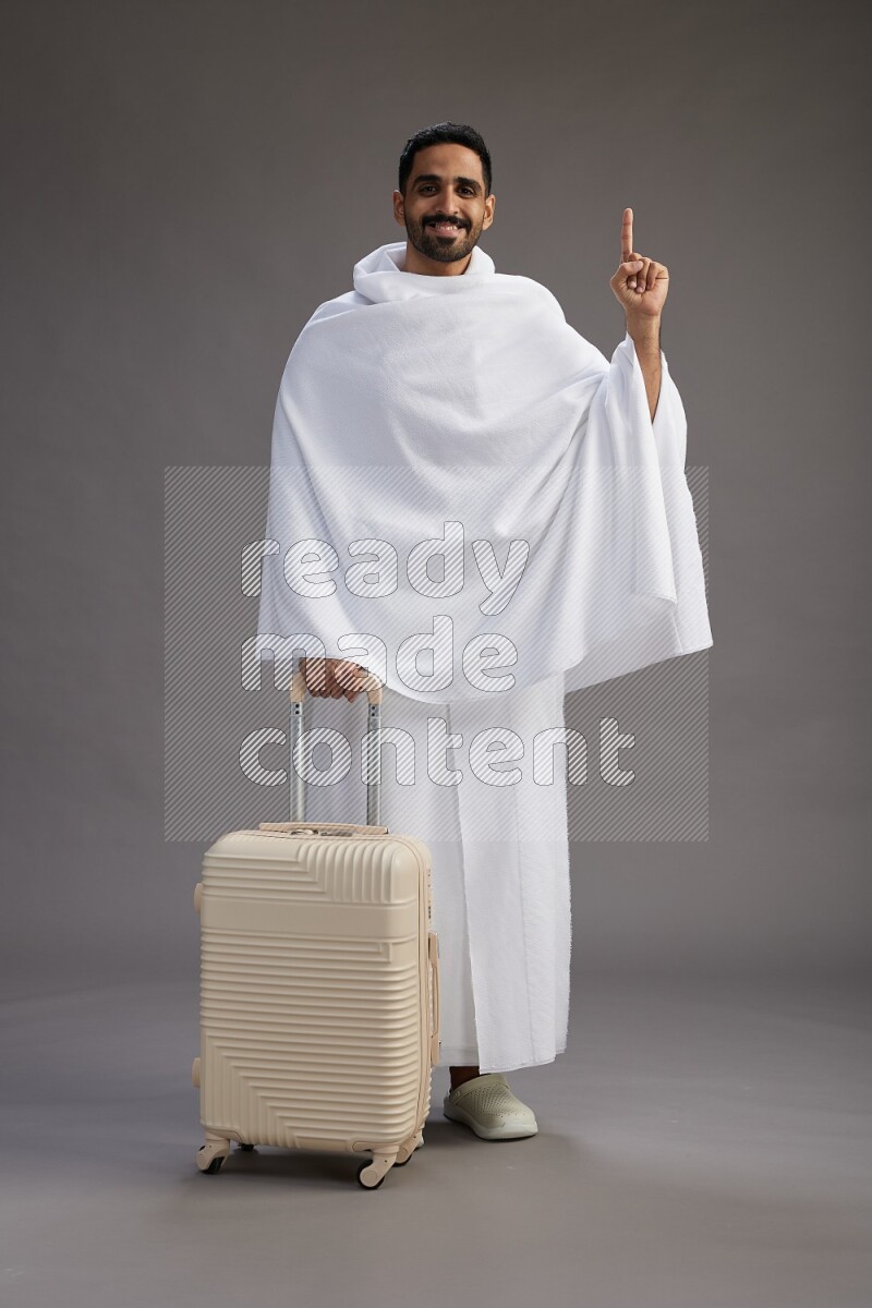 A man wearing Ehram Standing holding traveling bag on gray background