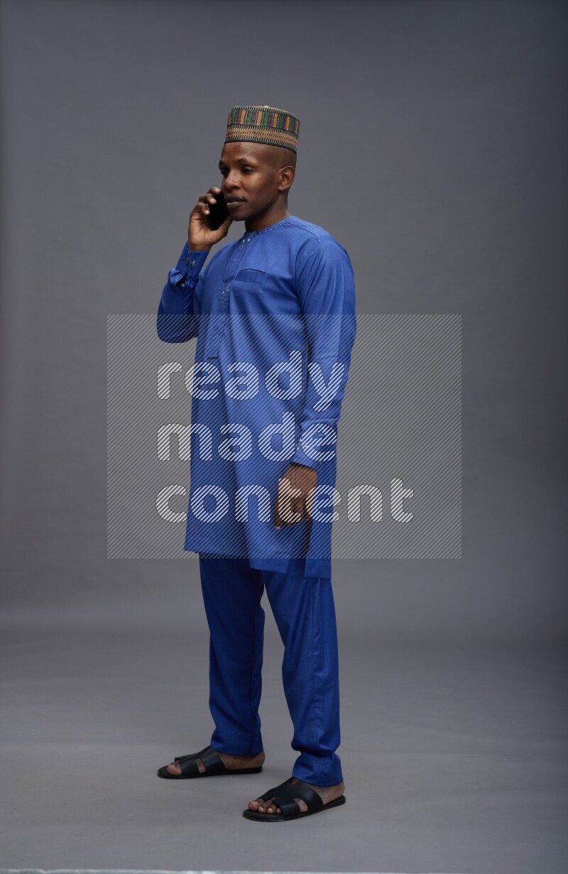 Man wearing Nigerian outfit standing talking on phone on gray background