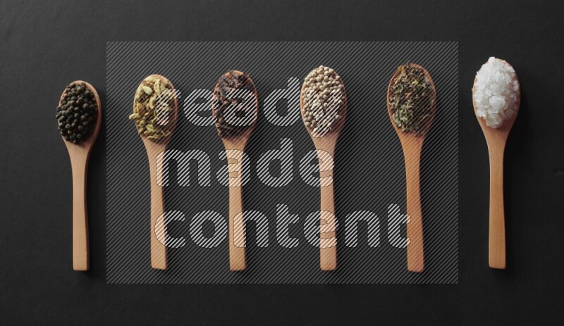 الفلفل الأبيض والقرنفل والهيل والملح والفلفل الأسود وريحان مجفف في معالق خشبية علي خلفية سوداء