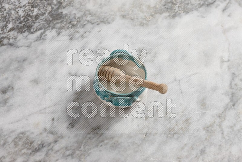 Multicolored pottery bowl with wooden honey dipper in it on grey marble background