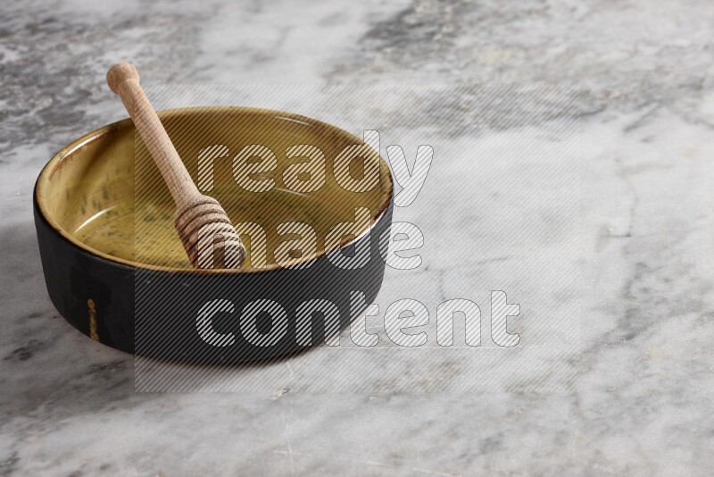 Multicolored Pottery Oven Plate with wooden honey handle in it, on grey marble flooring, 45 degree angel