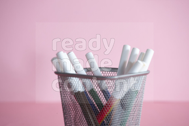 Pens, pencils and other different school supplies in a metal pen holder on rose background
