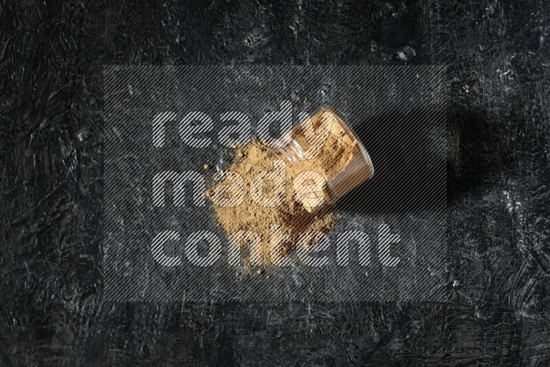 وعاء زجاجي مقلوب ممتلئ ببودرة بهار الفلفل الحلو والبودرة تناثرت منه على خلفية سوداء