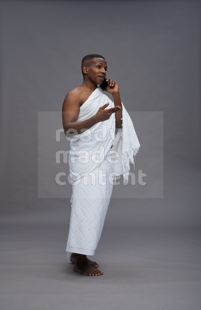A man wearing Ehram Standing talking on phone on gray background
