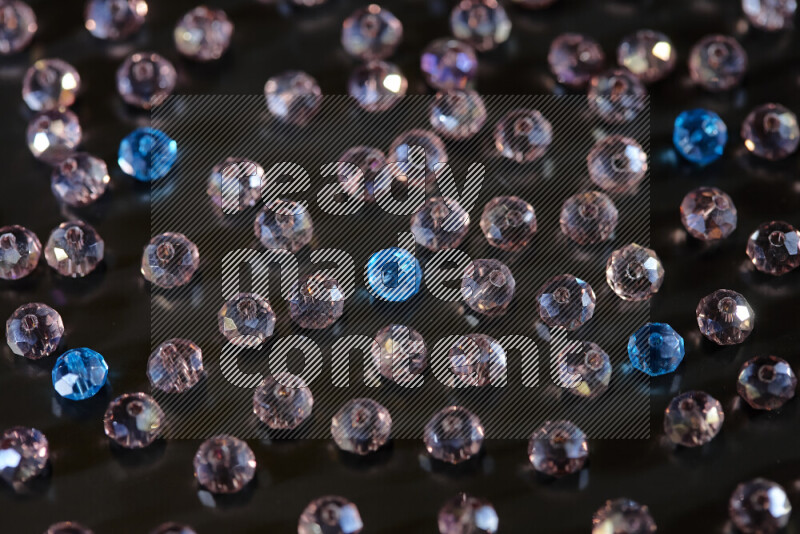 Rose and blue transparent crystal beads scattered on a black background