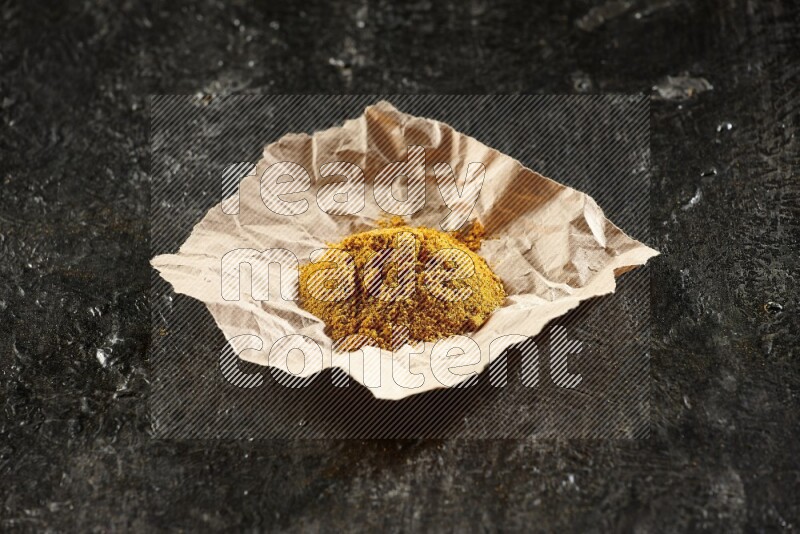 Turmeric powder in a crumpled piece of paper on textured black flooring