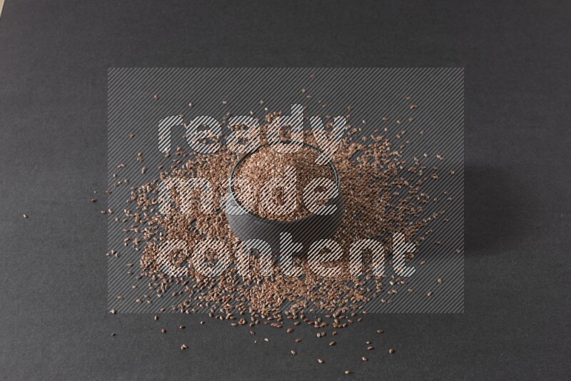 وعاء فخاري أسود ممتلئ بحبوب بذر الكتان محاط بالبذور على أرضية سوداء