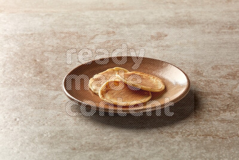 Three stacked plain mini pancakes in a brown plate on beige background