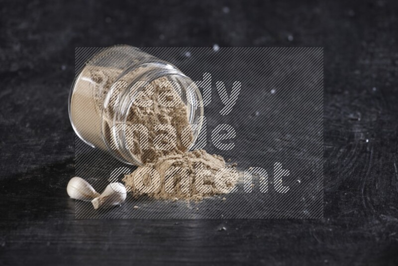 A glass jar full of garlic powder flipped over with the powder came out on a textured black flooring