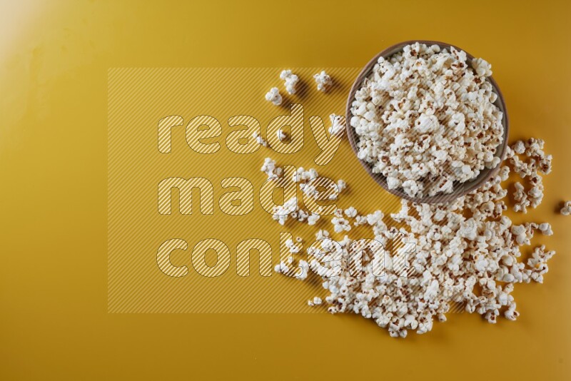 A brown pottery bowl full of popcorn with popcorn beside it on a yellow background in different angles