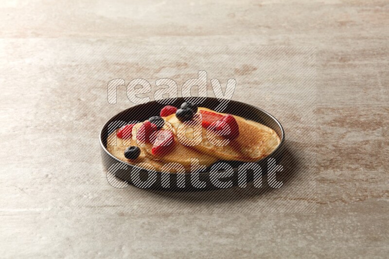 Three stacked mixed berries pancakes in a black plate on beige background
