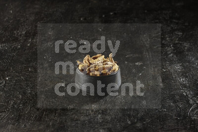 وعاء فخار أسود ممتلئ بأصابع كاملة من الكركم المجفف على خلفية سوداء