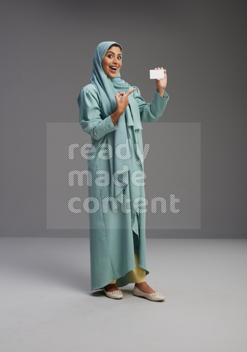 Saudi Woman wearing Abaya standing holding ATM card on Gray background
