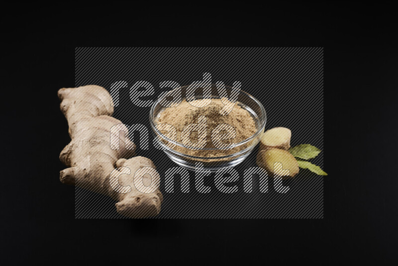 A glass bowl full of ground ginger powder on black background