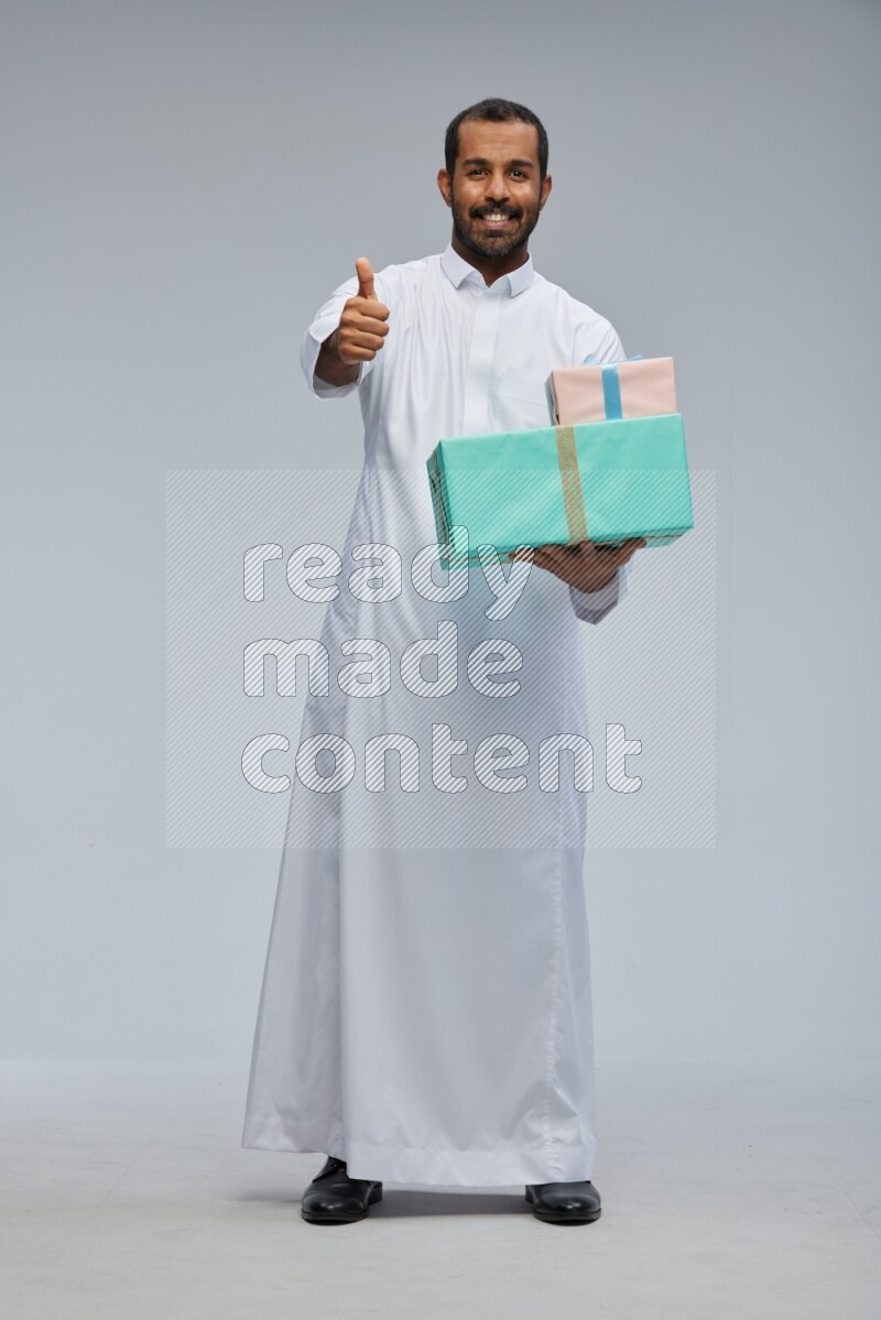 Saudi man Wearing thob standing holding gift box on Gray background