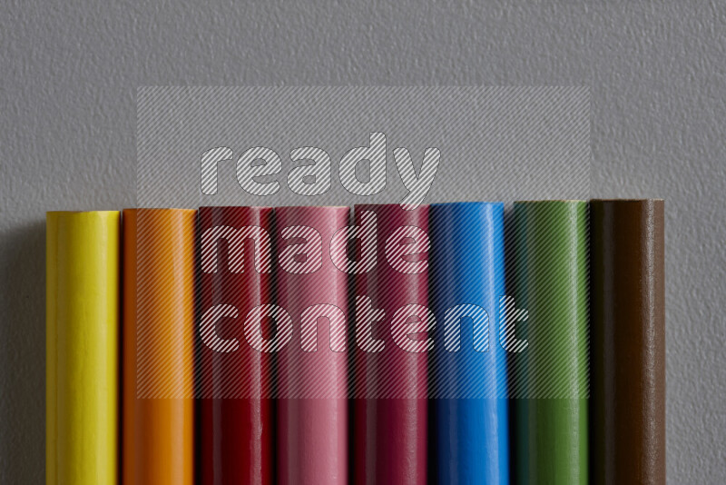 A collection of colored pencils arranged showcasing a gradient of different hues on grey background