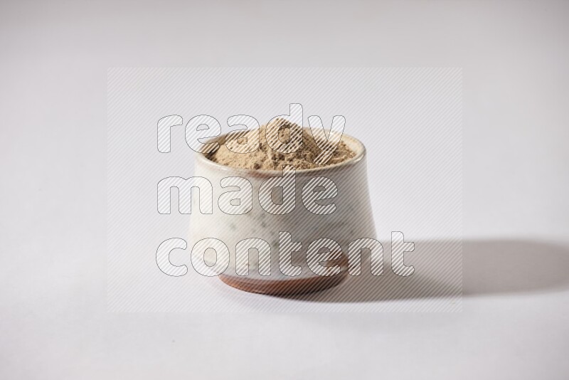 A beige pottery bowl full of garlic powder on a white flooring