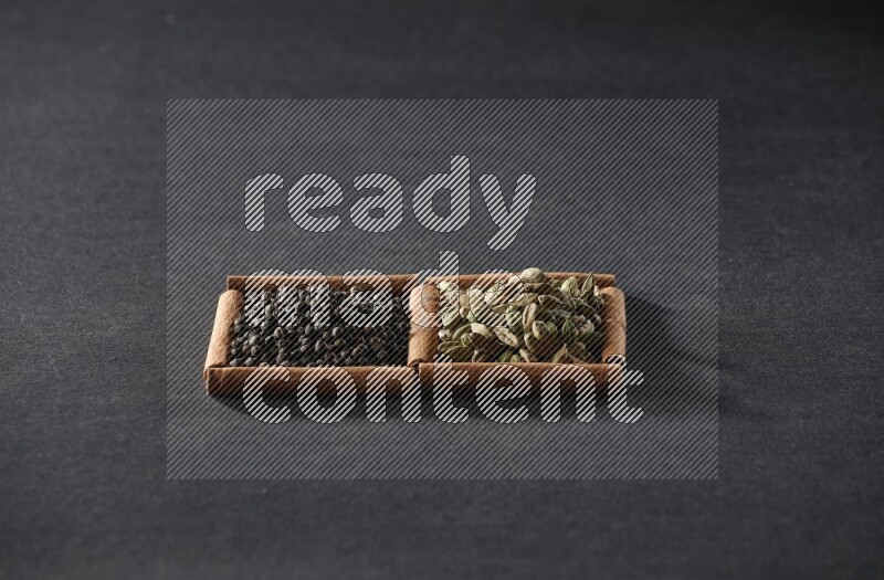 مربعان من أعواد القرفة ممتلئان بحبوب الفلفل الأسود وحب الهيل علي خلفية سوداء