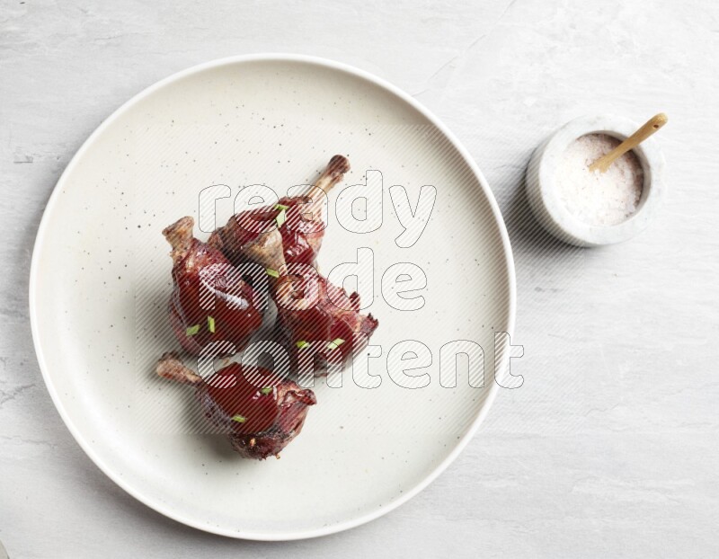 drumstick wrapped in bacon on round white ceramic plate on grey textured countertop