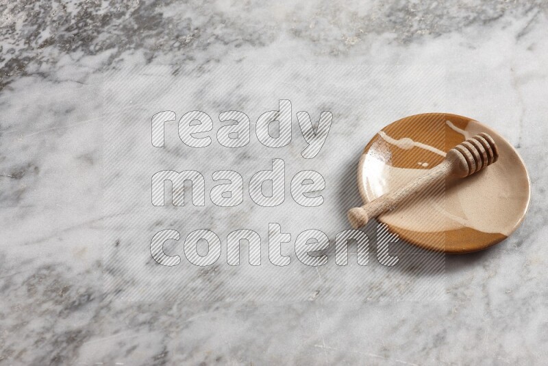 Multicolored pottery plate with wooden honey dipper in it on grey marble background