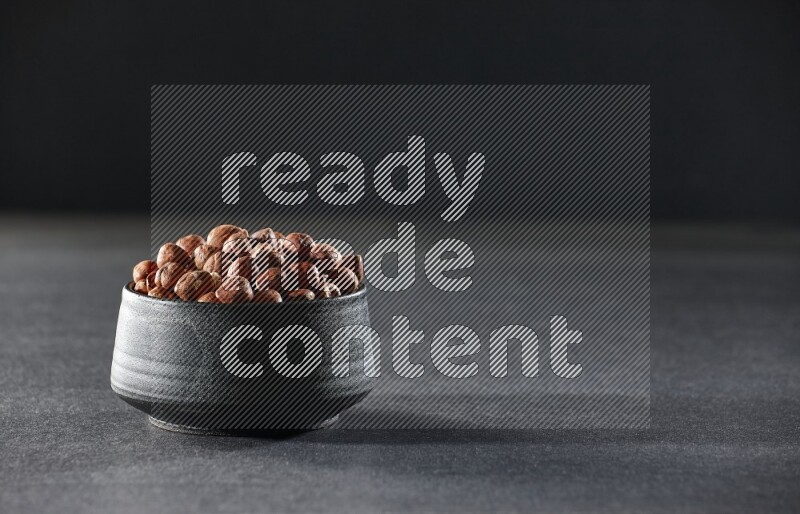 A black pottery bowl full of peeled hazelnuts on a black background in different angles