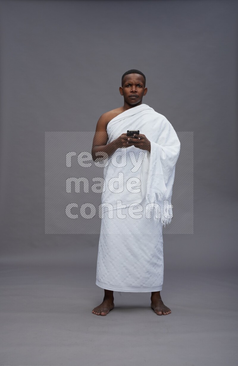 A man wearing Ehram Standing texting on phone on gray background