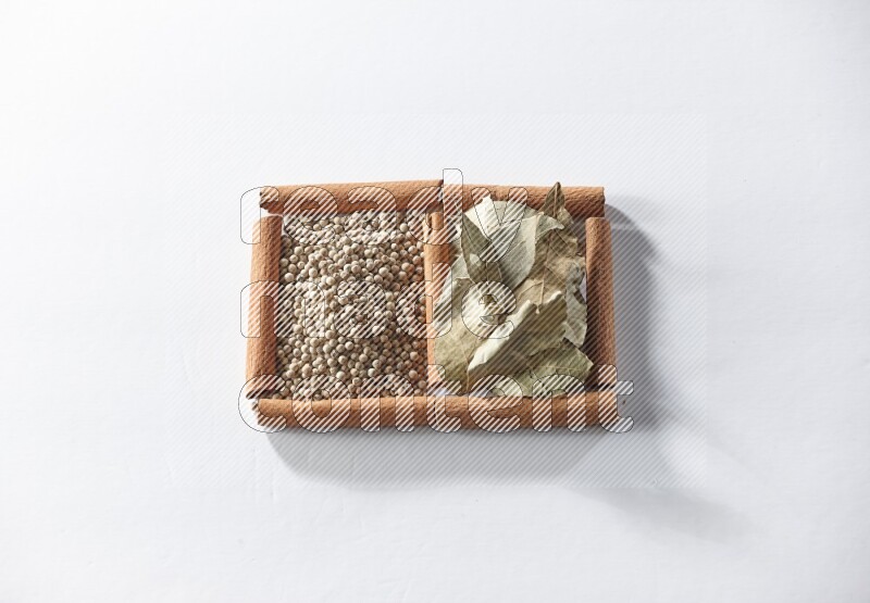 مربعان من أعواد القرفة ممتلئان بحبوب الفلفل الأبيض وأوراق الغار علي خلفية بيضاء