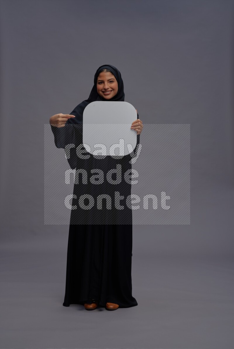 Saudi woman wearing Abaya standing holding social media sign on gray background