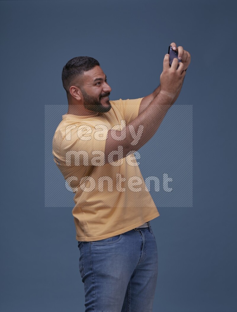 A man Playing Games on Smartphone on Blue Background wearing Orange T-shirt