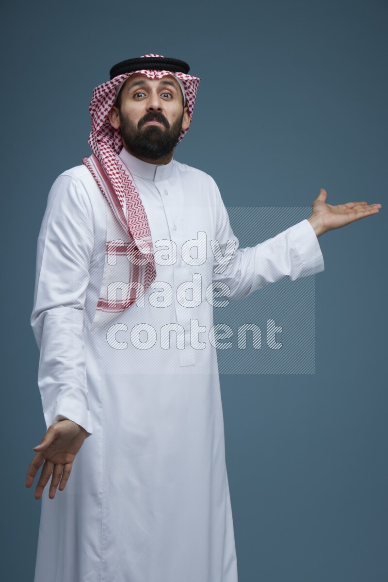 A man pointing in a blue background wearing Saudi Thob and Shomag