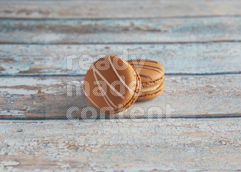 45º Shot of of two assorted Brown Irish Cream, and light brown Almond Cream macarons next to each other on light blue background