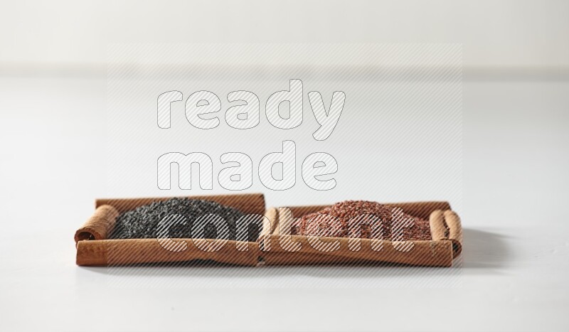 مربعان من أعواد القرفة ممتلئان بحبة البركة السوداء وبذور الكتان علي خلفية بيضاء