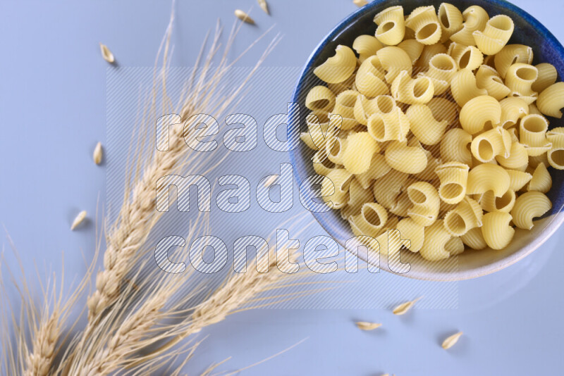 Raw pasta with wheat stalks on light blue background