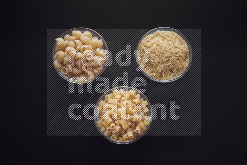 Different pasta types in glass bowls on black background