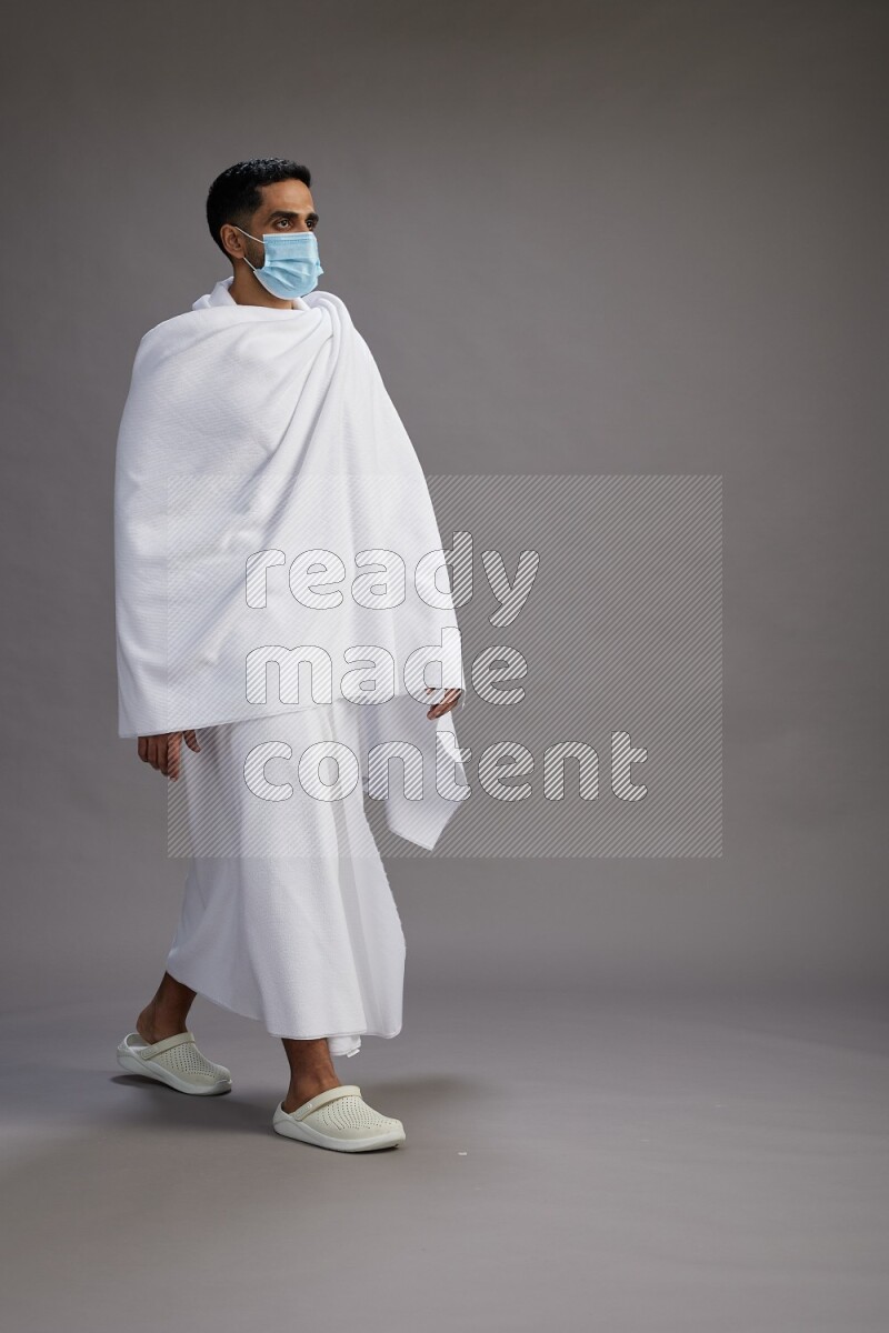 A man wearing Ehram with face mask Standing Interacting with the camera on gray background