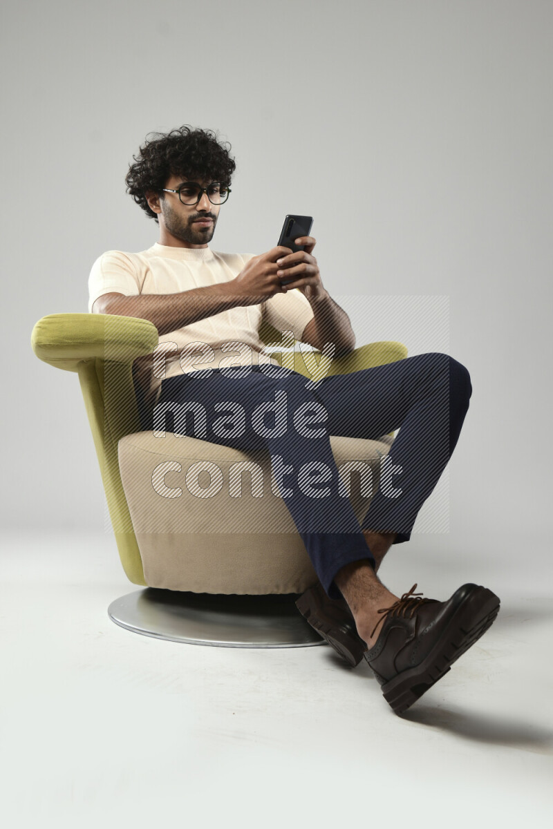 A man wearing casual sitting on a chair browsing on the phone on white background