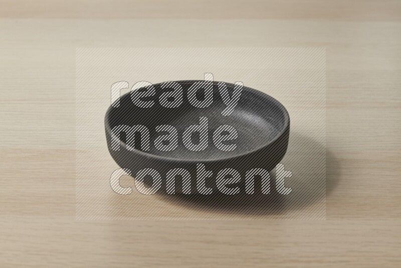 A black pottery bowl on light wooden background