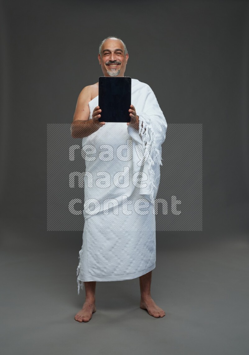 A man wearing Ehram Standing working on tablet on gray background