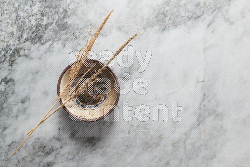 Wheat stalks on decorative pottery plate on grey marble background