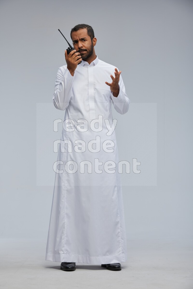 Saudi man Wearing thob standing holding walkie-talkie on Gray background