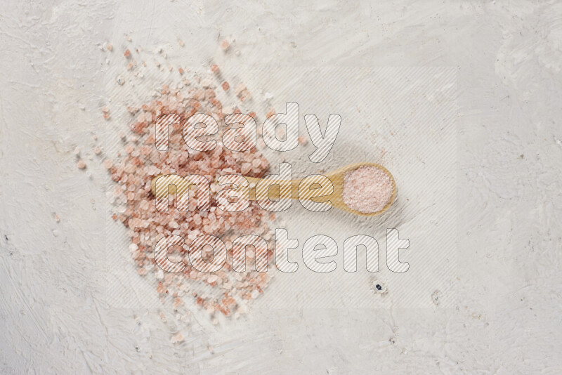 A wooden spoon full of pink himalayan salt on white background