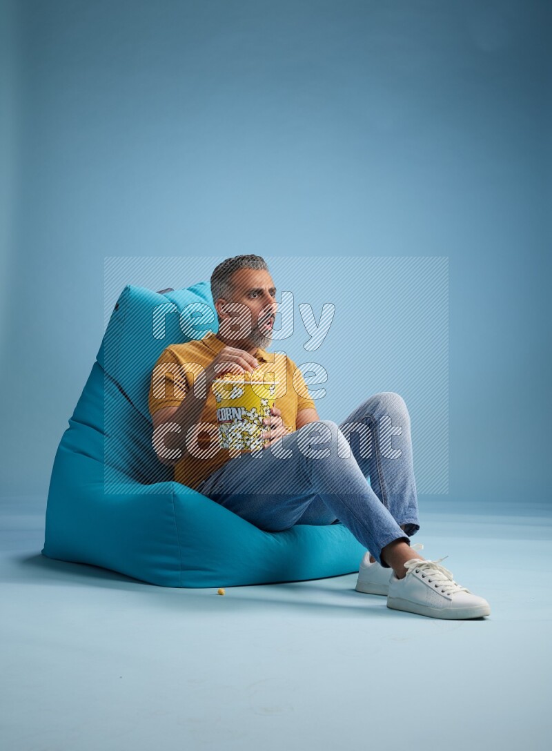 A man sitting on a blue beanbag and eating popcorn
