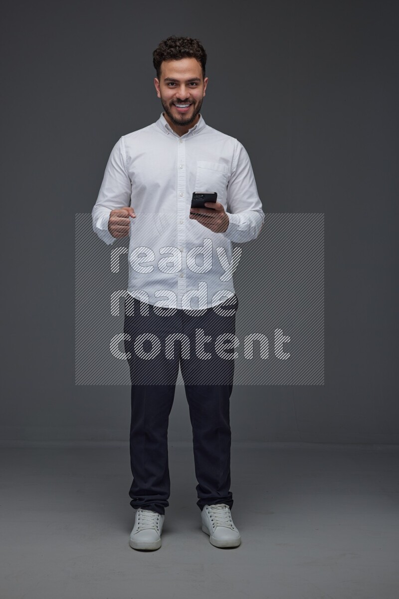 A man wearing smart casual standing and using his phone eye level on a gray background