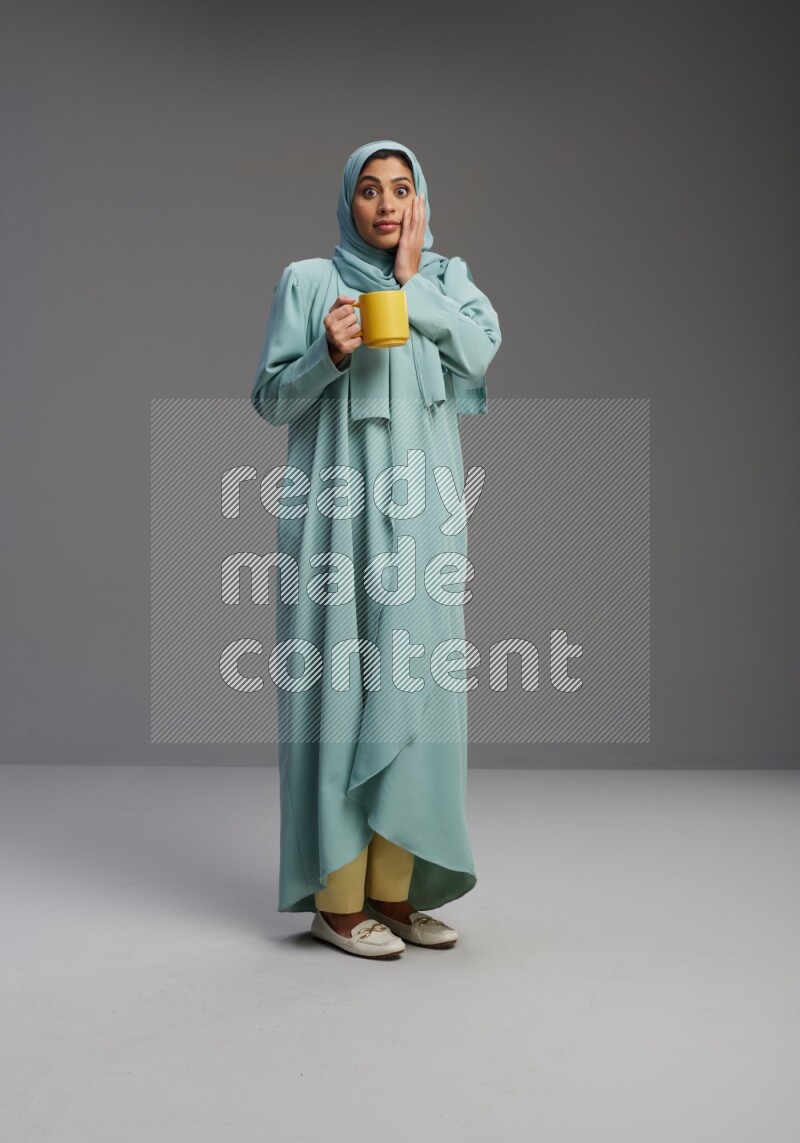 Saudi Woman wearing Abaya standing  holding a mug on Gray background