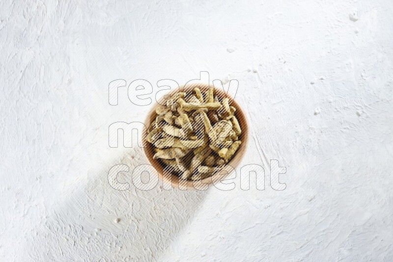 A wooden bowl full of dried turmeric whole fingers on a textured white flooring