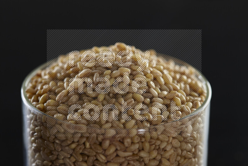 Hulled wheat in a glass jar on black background