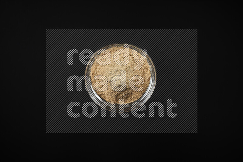A glass bowl full of ground ginger powder on black background