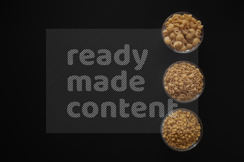 Different pasta types in 3 glass bowls on black background