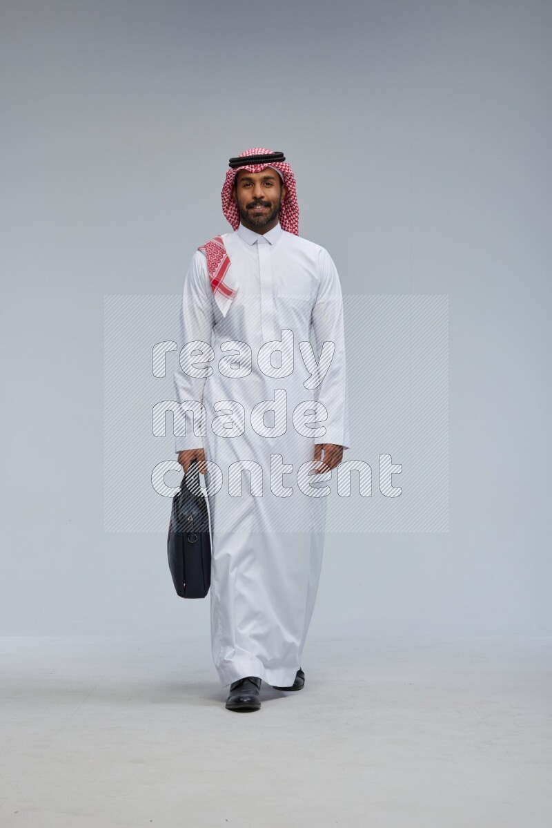 Saudi man Wearing Thob and shomag standing holding bag on Gray background