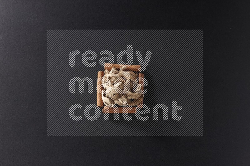 أربعة من أعواد القرفة مكونة شكل مربع بداخلها زنجبيل مجفف علي خلفية سوداء